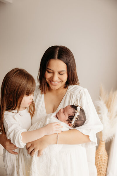 Lyla being held by her mother and sister during a newborn studio maternity photoshoot with michelle kelly photography