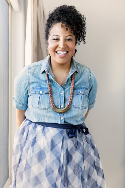 Women in front of a window with arms crossed behind her back.