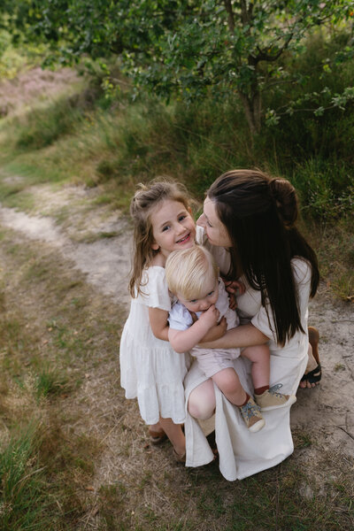 Foto van gezin met twee jonge kindjes die knuffelen in de duinen op het strand.