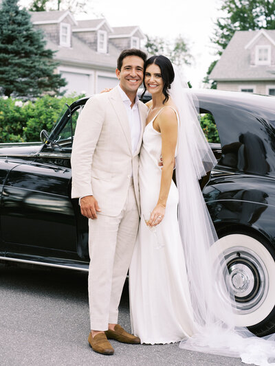 A bride and groom smiling in front of a classic car at their wedding in Boothbay Harbor, Maine
