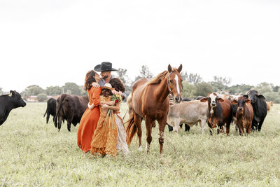 a family hugging with their horse next to them in front of a cow field