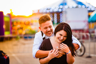 A engaged couple hugging in the warm glow of the sunset at the Michigan State Fair