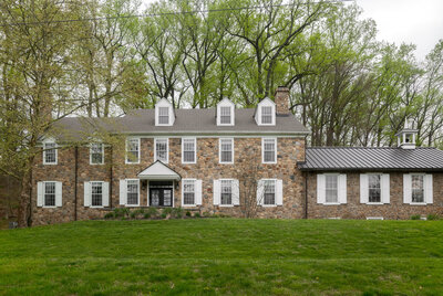 stone wall home with windows and white panel accents and green grass