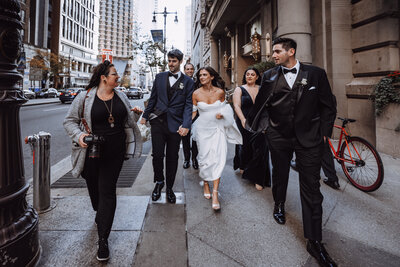 Kristen Catoe strides down a downtown philadelphia street talking to a bride and groom as they follow her