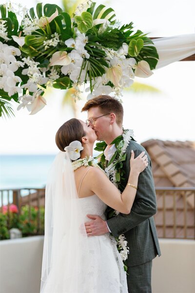 A wedding couple with their arms around each other as they kiss 