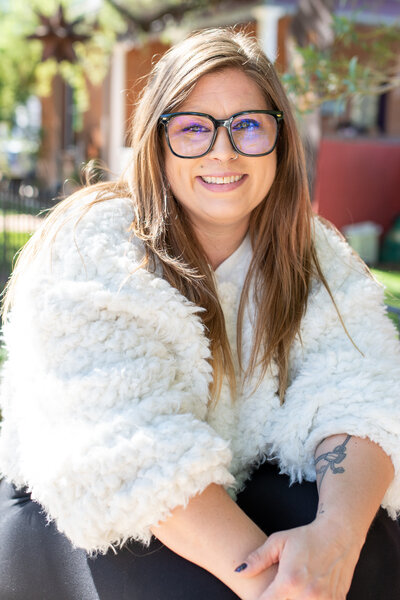 Smiling woman wearing glasses and a fluffy white sweater in a bright outdoor setting, photographed by Vyrl Photo, showcasing Tucson brand photography.