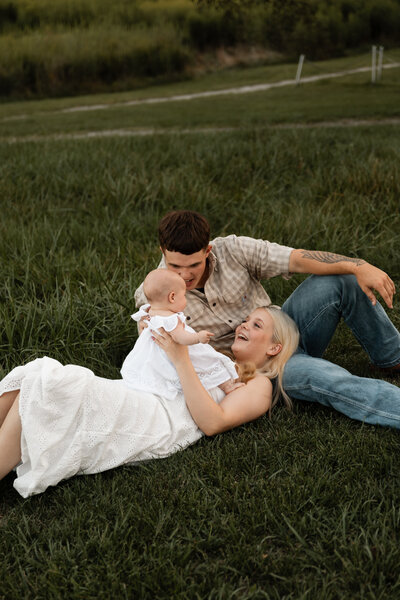 Couple lying with their baby together in a grassy field, enjoying a peaceful and intimate moment surrounded by nature, captured in a serene outdoor setting.