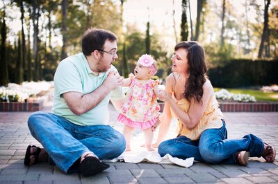 Parents helping their baby girl stand during a playful outdoor family photo session in Orlando, Florida.