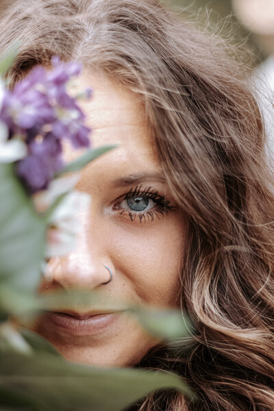 This image captures the beauty of a young womans blue eye peeking behind a bouquet of flowers.