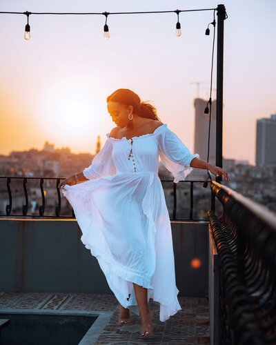 Woman dances in a white dress on a rooftop at sunset
