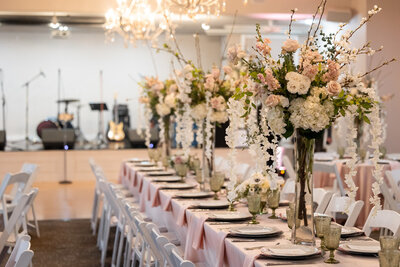 an elegantly set wedding reception table adorned with tall floral centerpieces, showcasing soft pastel flowers.