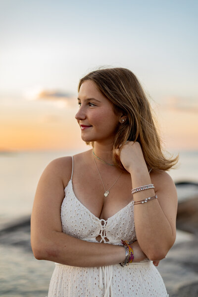 Image of senior girl playing with her hair looking off to the side in a sunset beach setting