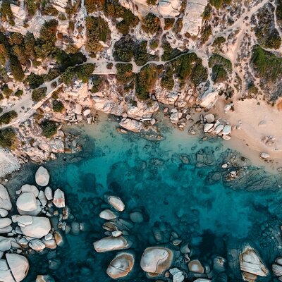 Aerial view of a rocky Mediterranean-style cove with turquoise blue water and sandy shoreline.