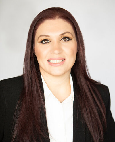 Headshot of woman with long brown hair and brown eyes wearing a black suit jackets over a white button down