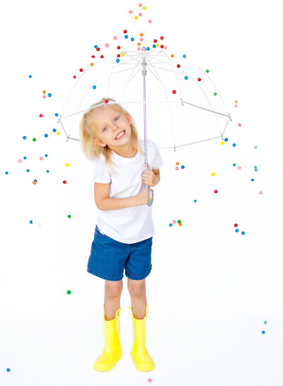 Little girl with a clear umbrella and yellow rainboots with gumballs falling down