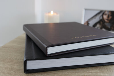 side picture of two leather-covered wedding albums, personalized on the bottom, with a small framed white print on the side of an Indian bride as a candle flickers in the background.