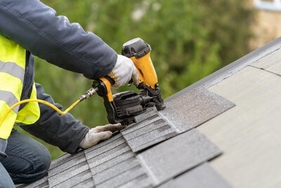 Worker installing shingles with nail gun.