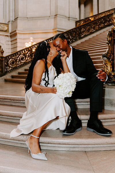 newlyweds smile and sit on city hall staircase