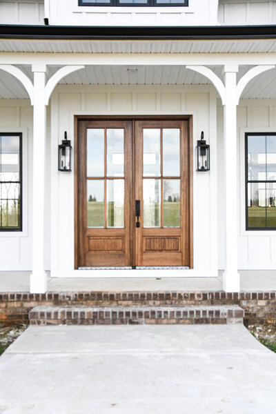Modern farmhouse white exterior siding, wooden front double doors, front porch.