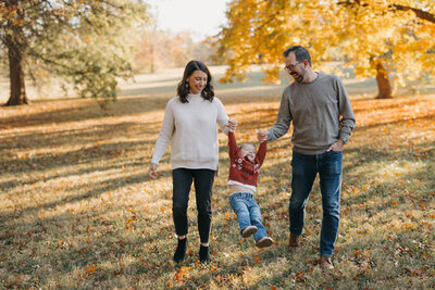 Brunette mother and father swinging daughter at park