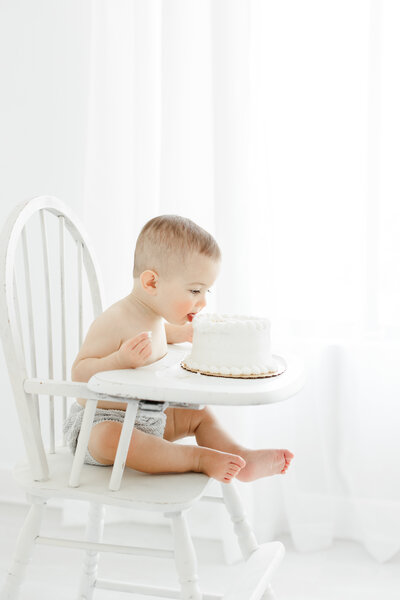 One year old baby boy celebrates his first birthday by trying cake for the first time at a cake smash photography session