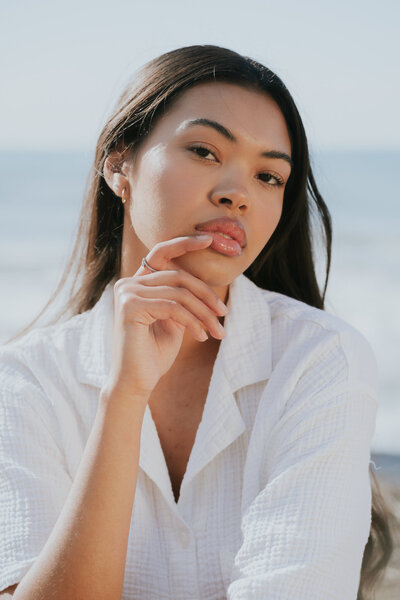 Portrait of woman holding her hand and extended finger over her lips wearing a white button up tshirt