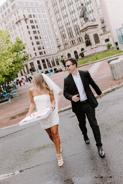 Man and woman walking down a sidewalk while holding hands and smiling at each other