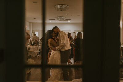 A view through the window of the wedding couple dancing at their reception.