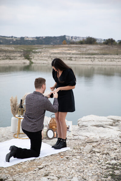 An Austin wedding photographer captures a picturesque moment as a woman proposes to a woman by the serene lake.