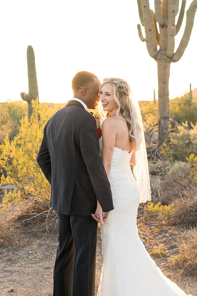 bride and groom laughing together as they pose for pictures in the desert with cactus