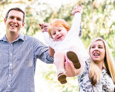 parents swing child in pink shorts between them