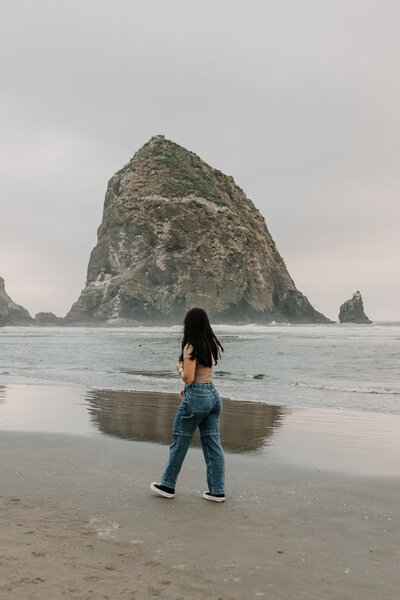 Brooke Pitchford wearing blue jeans and sneakers walking down the beach towards haystack rock