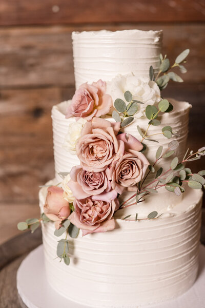 White wedding cake decorated with blush roses and eucalyptus