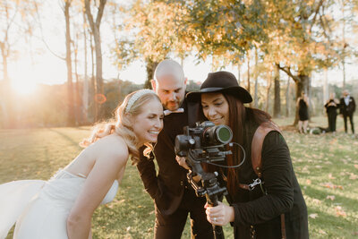 Tashina Narelle shows a bride and groom the back of her camera so they can see the video she just captured of them at sunset on their wedding day.