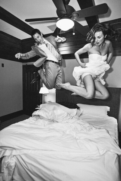 Newlyweds jumping on teh bed at West shore cafe in Lake Tahoe. black and white image of bride and groom 