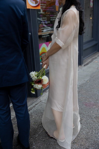 A woman wearing a sheer white wedding dress holding a vibrant bouquet of flowers