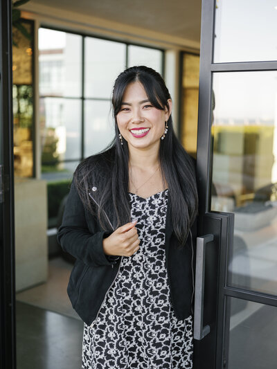 A woman standing in front of glass windows and doors and smiling during sunset