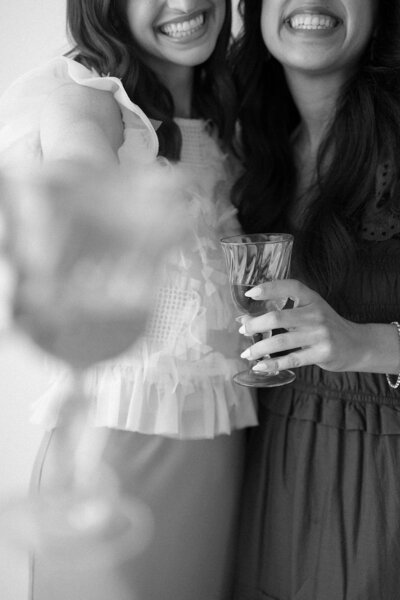 Black and white image of two women in fancy outfits holding drink glasses