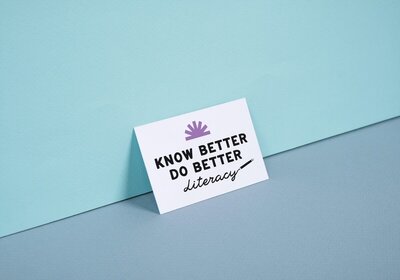 Know Better Do Better Literacy business card leaning against a blue wall