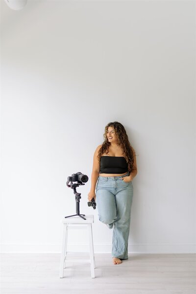 Lifestyle branding portrait of Hiba, Raleigh wedding photo and video artist, standing with her camera in natural light studio.
