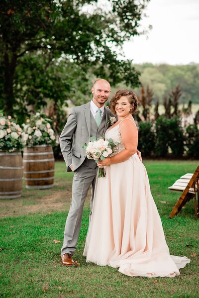 Bride wearing blush dress standing with her husband and smiling at the camera outside of their venue