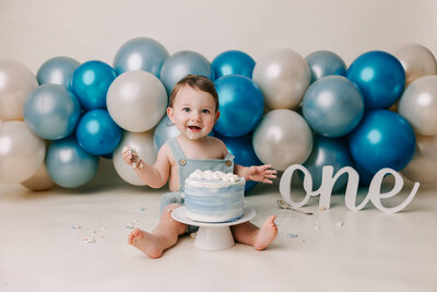 Baby boy in blue overalls eating cake in PDX studio