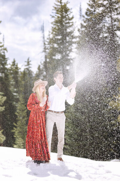 a couple spray champagne on top of aspen mountain after she said yes to a marriage proposal