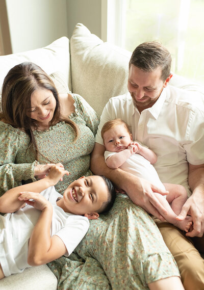 Parents and siblings laugh together on a cozy couch, sharing a joyful family moment. A heartfelt family session by Moments in Light Photography.