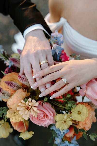man and woman holding hands with rings on bride's bouquet