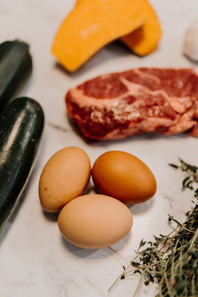 Three eggs on the counter next to herbs and meat