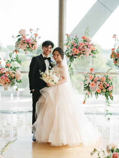 A couple walks on a rooftop on their wedding day, holding an Anthousai bouquet.
