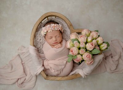 Baby girl sleeping in a heart crate with a pink swaddle and pink roses. Studio newborn photoshoot in Woodstock GA, outside of Atlanta, GA.
