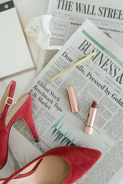 Red heels and lipstick laying on top of a newspaper