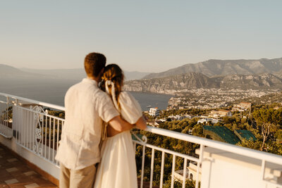 a couple overlooking the mountains of the amalfi coast in italy with their backs toward the camera.